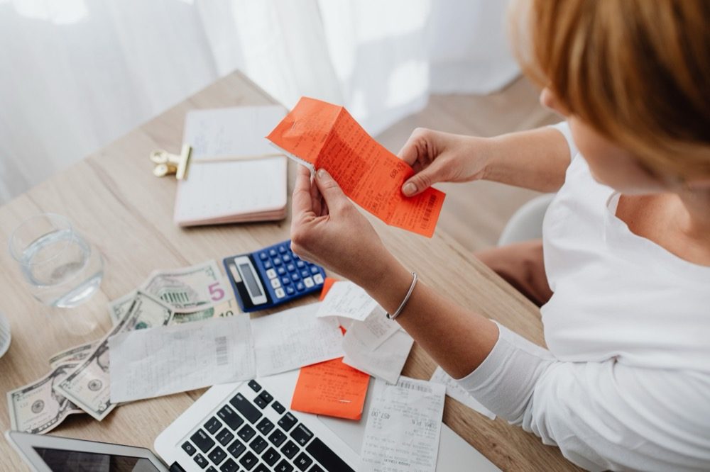 A small business owner totaling receipts with a calculator at a desk