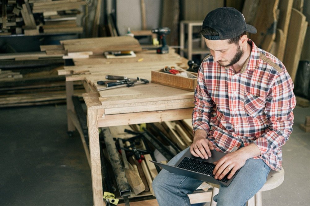 Carpenter checking his website on a laptop in his workshop